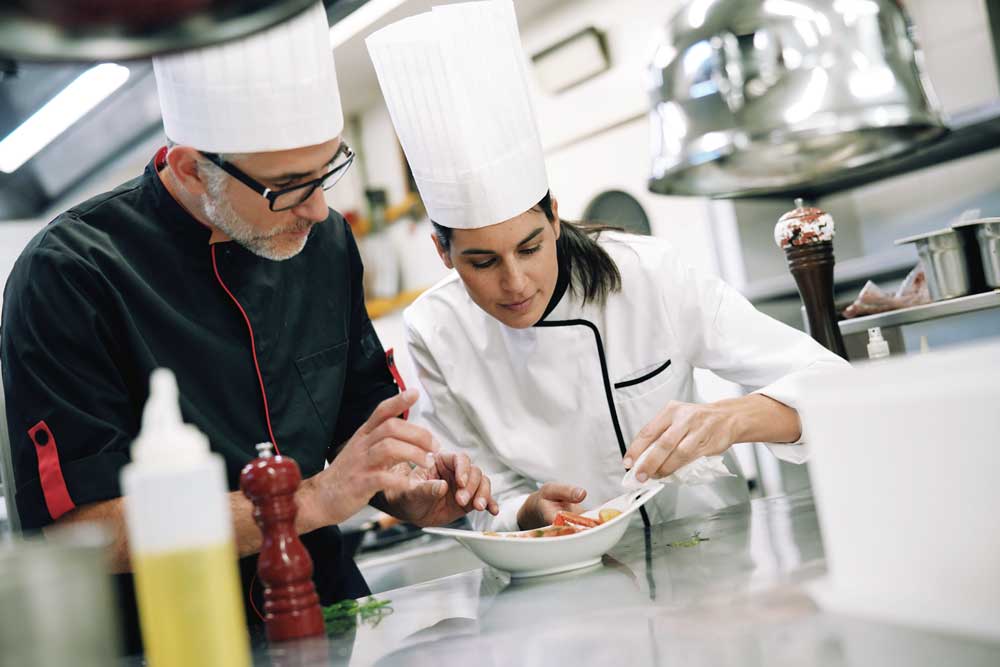 Betriebsübergabe mit Liegenschaften – was ist zu beachten? - Immobilien - Professional cook chefs in kitchen improving dish composition
